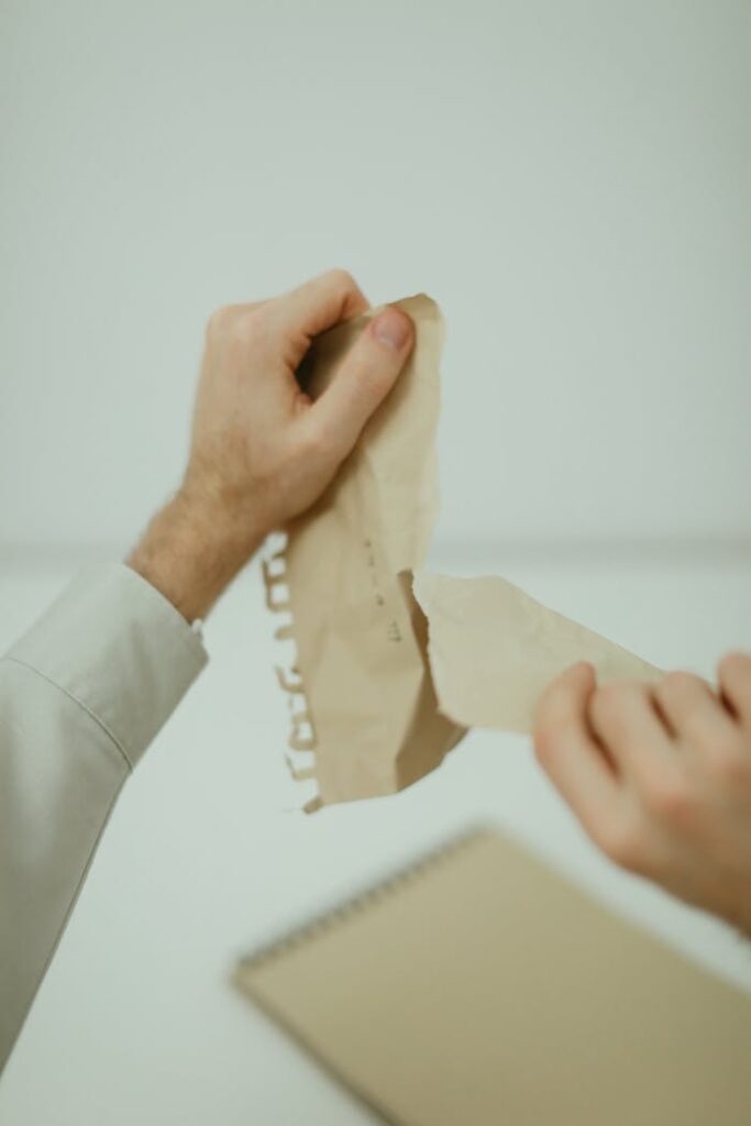 Close-up of hands tearing brown paper indoors, symbolizing waste disposal.