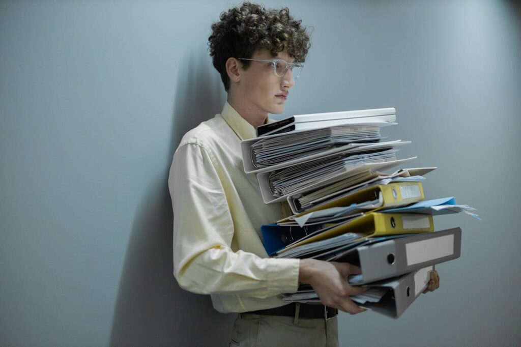 pexels-photo-8468119 An overworked office worker carrying a large stack of files and folders in a modern setting.