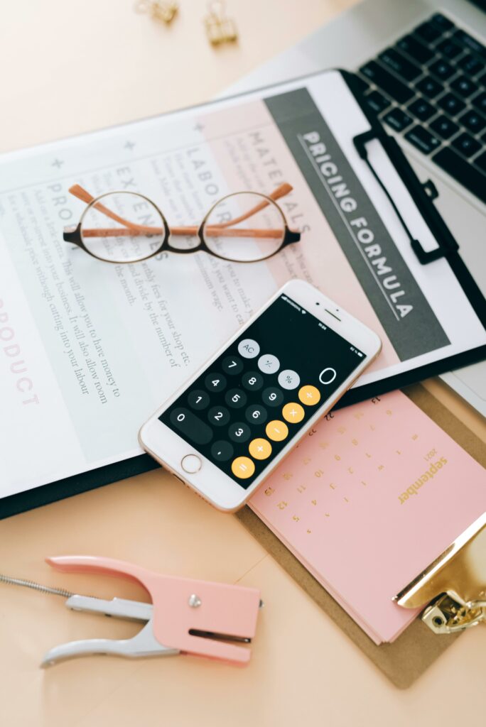 Flat lay of business tools including smartphone, calculator, and eyewear on a desk.