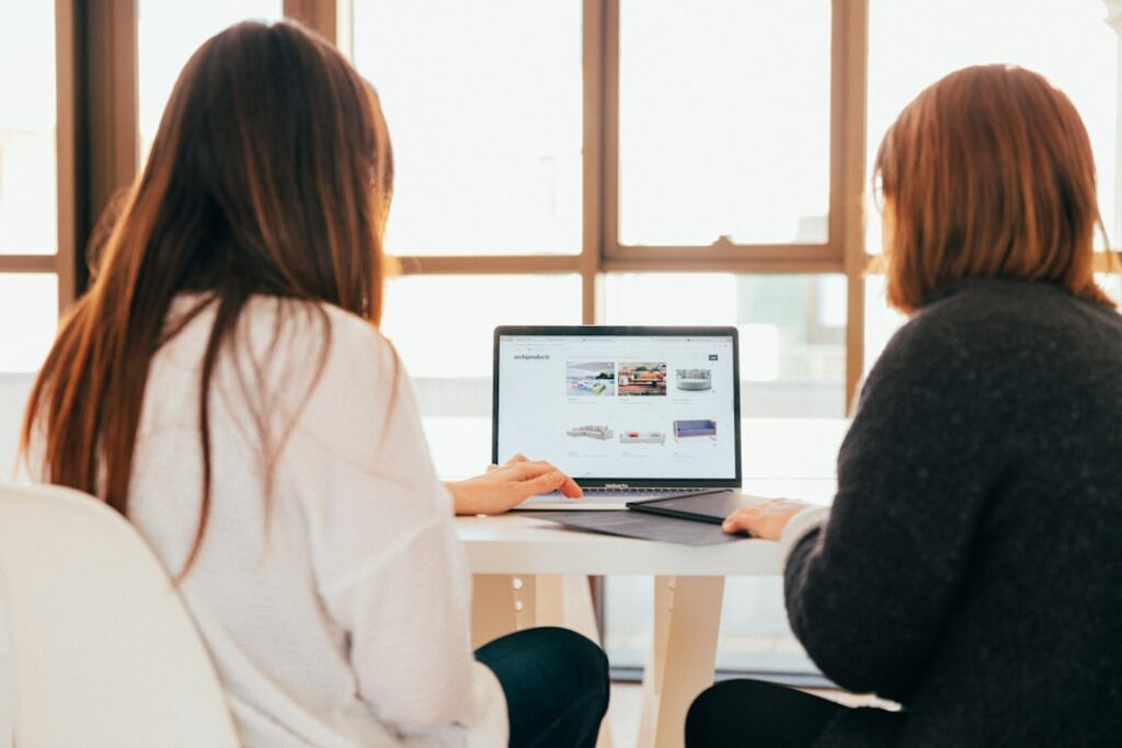 two-women-talking-while-looking-at-laptop-computer-7okkfhxrxnw